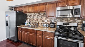 A kitchen with wooden cabinets, stainless steel appliances, a tiled backsplash, and a granite countertop. - The Rock House (Big Bear City)