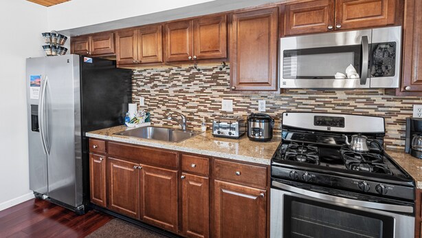 A kitchen with wooden cabinets, stainless steel appliances, a tiled backsplash, and a granite countertop. - The Rock House (Big Bear City)