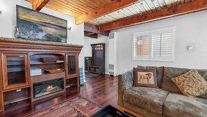 A living room with a fireplace, wooden cabinets, a sofa with patterned cushions, and a painting on the wall. - The Rock House (Big Bear City)