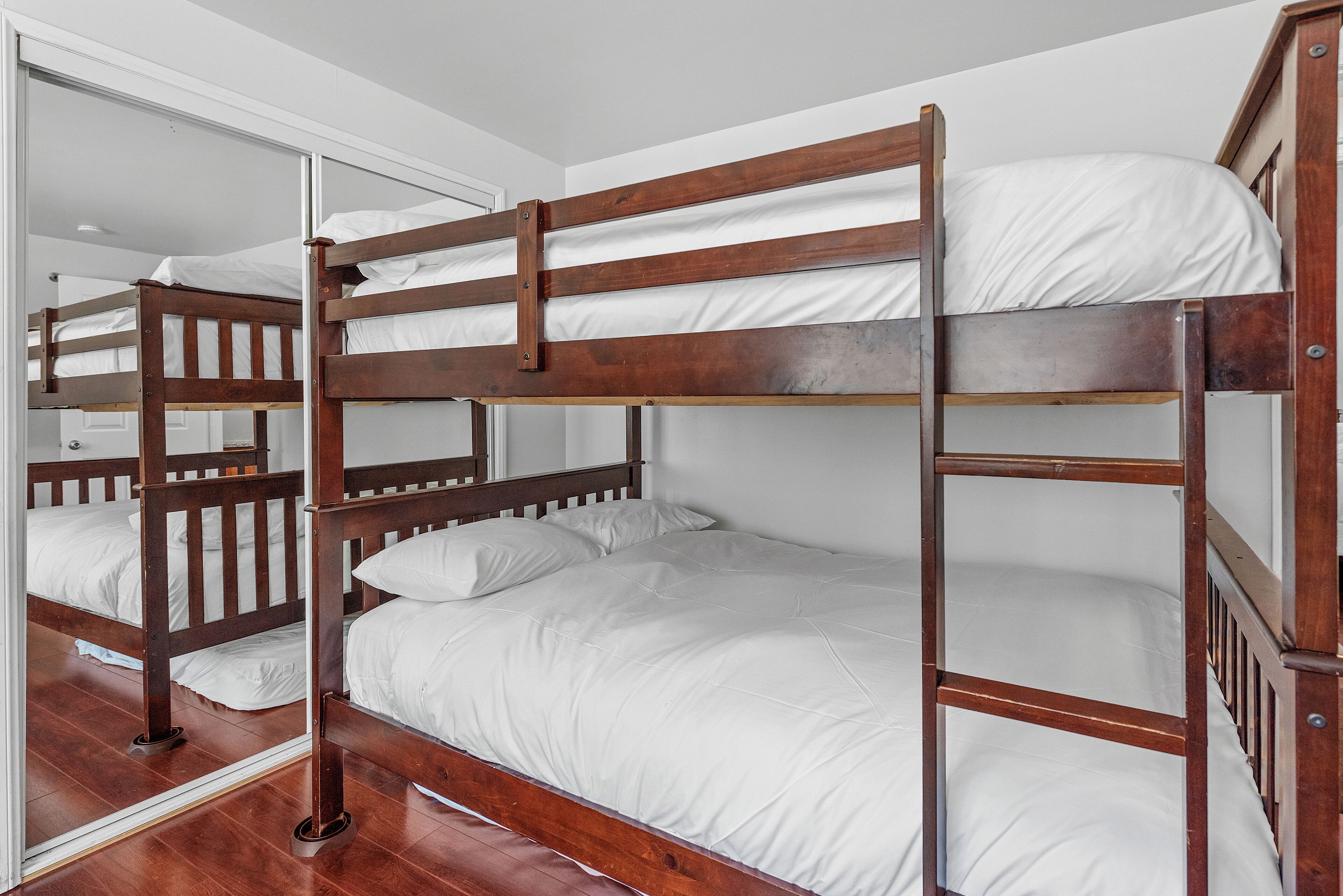 Una cama litera con ropa de cama blanca en una habitación con suelo de madera y paredes blancas.
