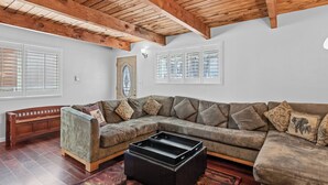 A living room with a sectional sofa, a wooden bench, and a black ottoman. - The Rock House (Big Bear City)