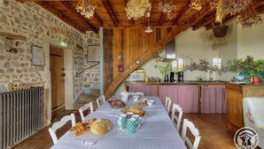 Comedor rústico con pared de piedra, techo de madera y una larga mesa dispuesta para el desayuno.