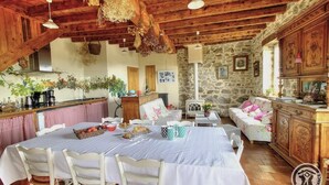 Una cocina rústica con paredes de piedra, vigas de madera y un comedor con sillas blancas y una mesa dispuesta para cuatro.