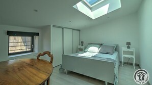 A bedroom with a skylight, a bed, bedside tables, a wooden chair, and a dining table.