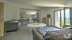 A spacious living area with a sofa, a coffee table, and a TV. There is a balcony with a view.