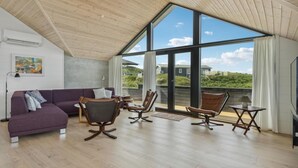 Una habitación amplia con techo alto, ventanas grandes, un sofá morado y sillones de cuero.