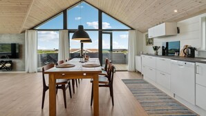 Una cocina moderna con un ventanal grande, techo de madera y un comedor con mesa y sillas.