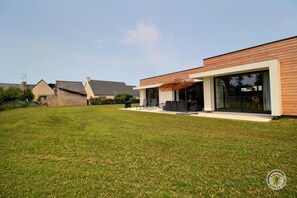 Una casa moderna con un patio amplio, mobiliario exterior y un césped cuidado.