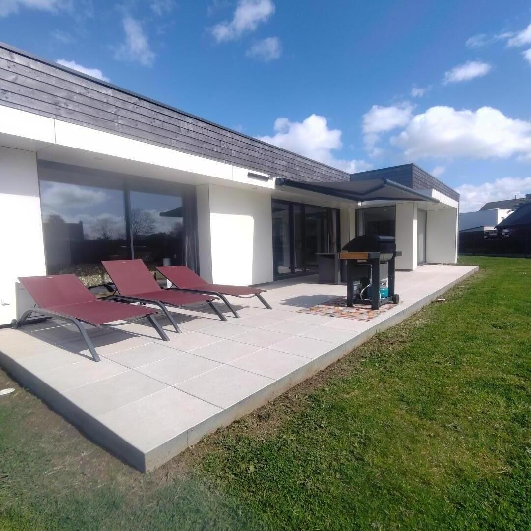 Une maison moderne dotée d’un patio, de deux fauteuils rouges et d’un barbecue.