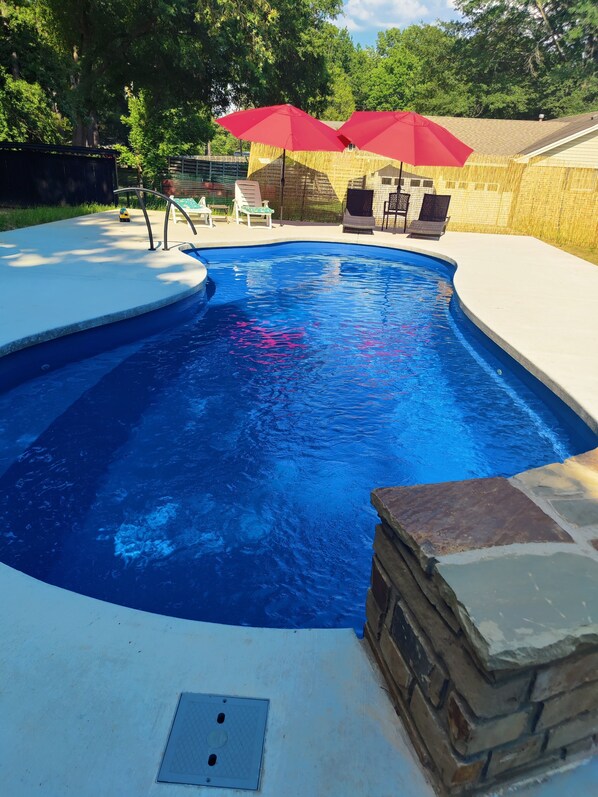 Relax by the pool surrounded by a deck and a stone accent wall, with comfortable seating and a grill nearby.