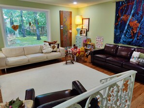 Relax in this serene space with a view of the lush garden, featuring a comfortable sofa and leather couch.