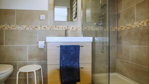 Uma casa de banho com sanita, lavatório com toalha e chuveiro.