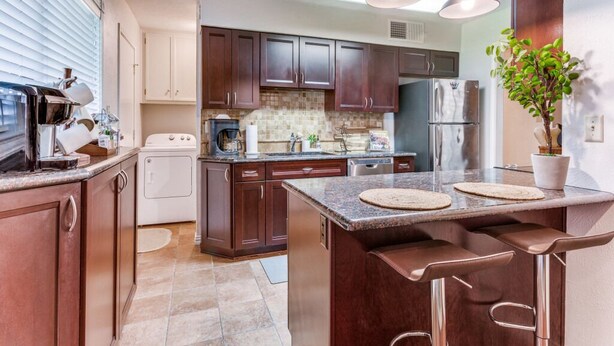A modern kitchen with dark wood cabinets, a central island with bar stools, a built-in oven, and a refrigerator. - Escape to Olivia's Hideaway in Allen! Close  to shopping,Eat, and entertainment (Allen)
