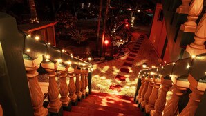 A staircase with wooden balusters and string lights, leading to a covered area with palm trees.