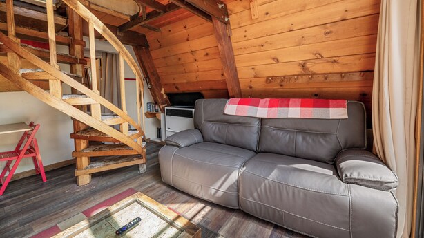 Interior acolhedor de uma cabana com escada de madeira, um sofá de couro e uma pequena mesa com um controle remoto.