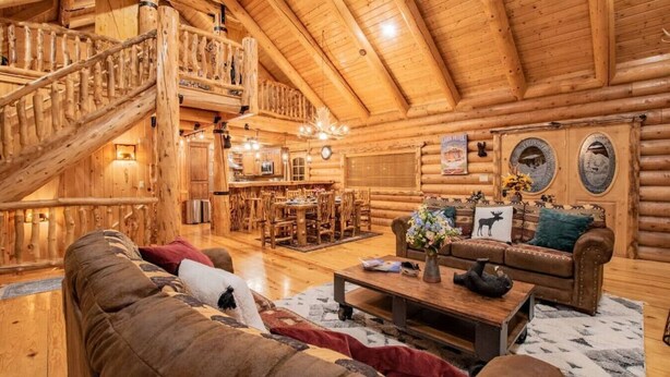 A log cabin interior with a wooden staircase, a dining area, and a living room with a sofa and coffee table. - The Moose & Bear Cabin at Timpanogos (Highland)