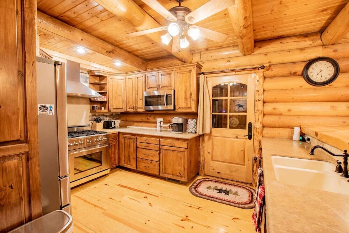 A wooden cabin interior with a kitchen featuring a refrigerator, stove, microwave, and wooden cabinets.