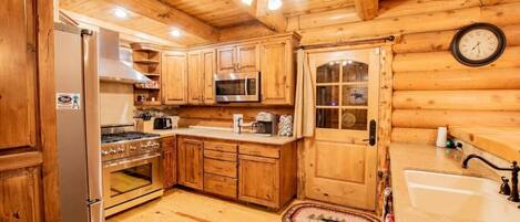A wooden cabin interior with a kitchen featuring a refrigerator, stove, microwave, and wooden cabinets.