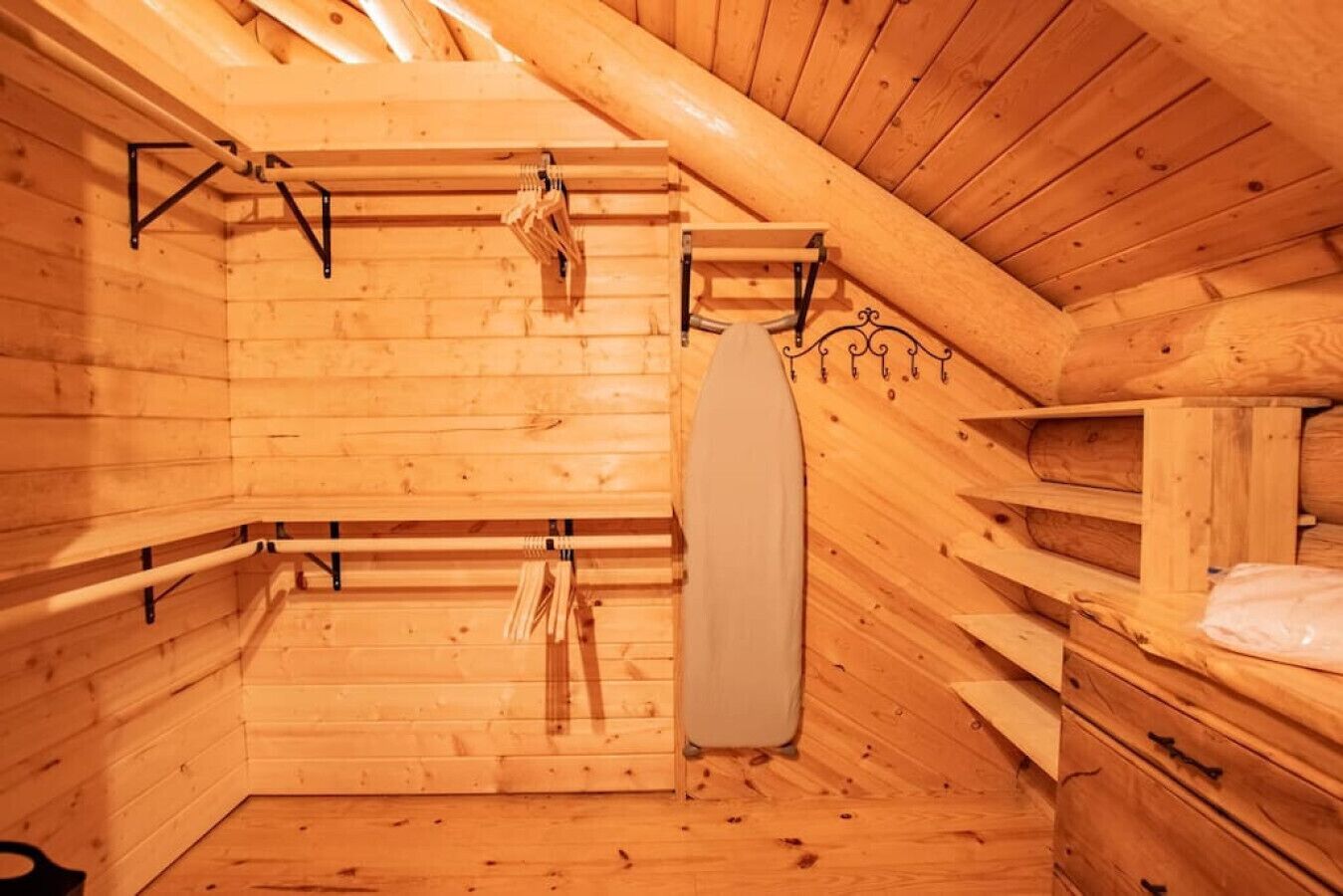 A wooden cabin interior with a loft bed, a hanging rack, and a small storage unit.