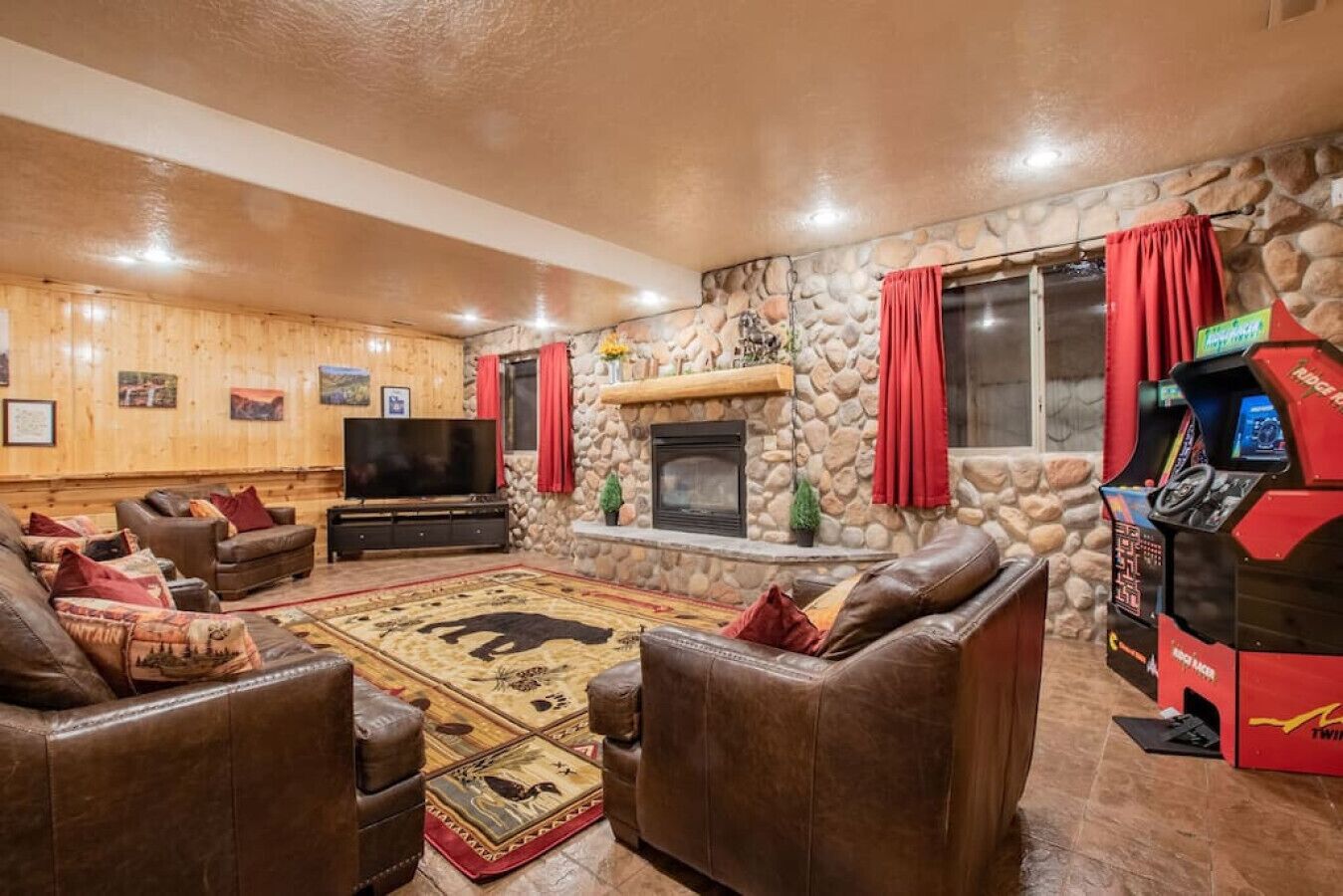A cozy living room with leather sofas, a flat-screen TV, a stone fireplace, and a red arcade machine.