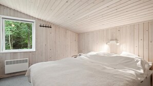 Un dormitorio con techo de madera, un ventanal con vistas a árboles, una cama con ropa blanca y un calentador de pared.
