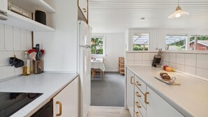 Una cocina moderna con armarios blancos, una isla central y un área de comedor visible a través de un umbral abierto.