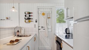 Una cocina con armarios blancos, un lavamanos de acero inoxidable, una tetera y botellas de vino en una estantería.