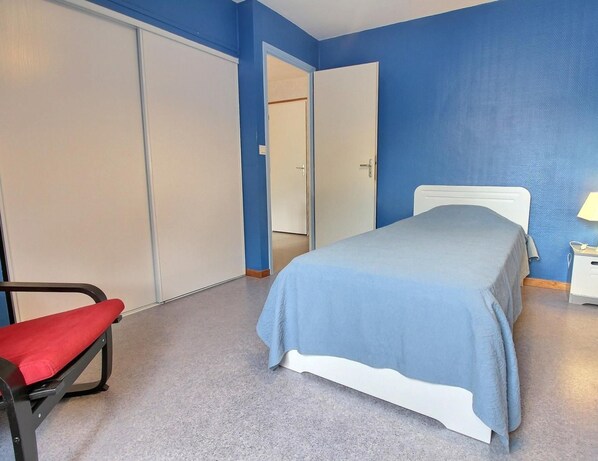 A bedroom with a bed, a chair, a nightstand with a lamp, and a wardrobe. - AR Gwenn KEV - Bono (BONO (LE))
