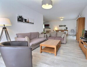 A modern living room with two sofas, a coffee table, a TV stand with a flat-screen TV, and a lamp.