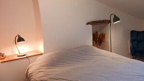 A bedroom with a bed, a desk lamp, a chair, and a window.
