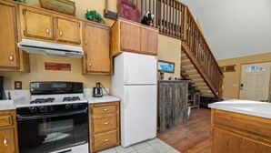 A kitchen with wooden cabinets, a white refrigerator, a stove, and a wooden staircase leading to another level. - The Outdoors Inn (Big Bear Lake)