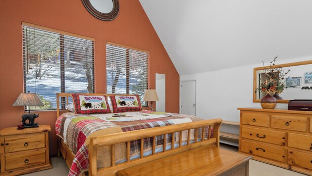 A bedroom with a wooden bed, two bedside tables, a dresser, and a large window with blinds. - The Outdoors Inn (Big Bear Lake)