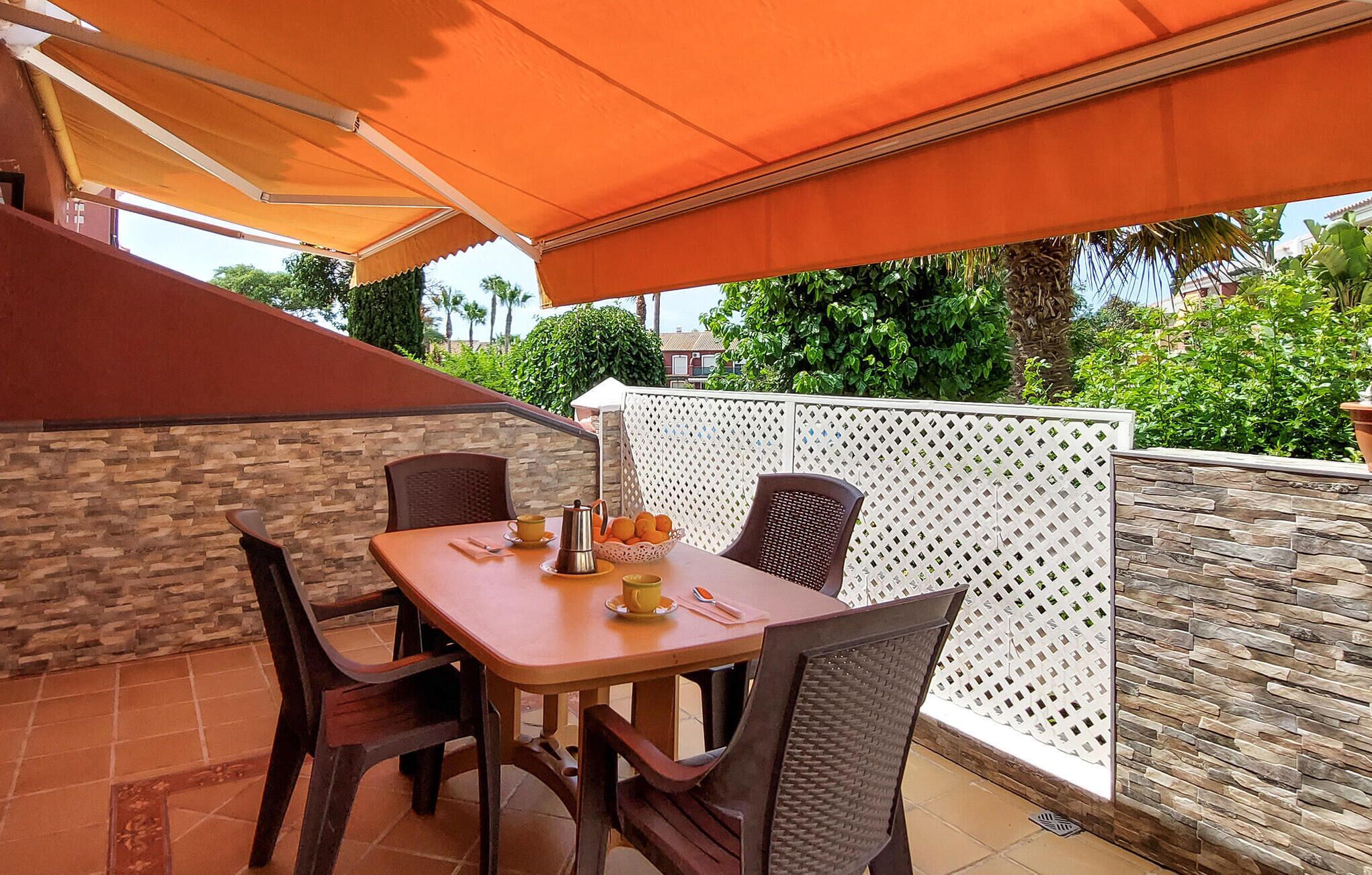 Une terrasse avec une table et des chaises, une cafetière et un panier rempli d’oranges.