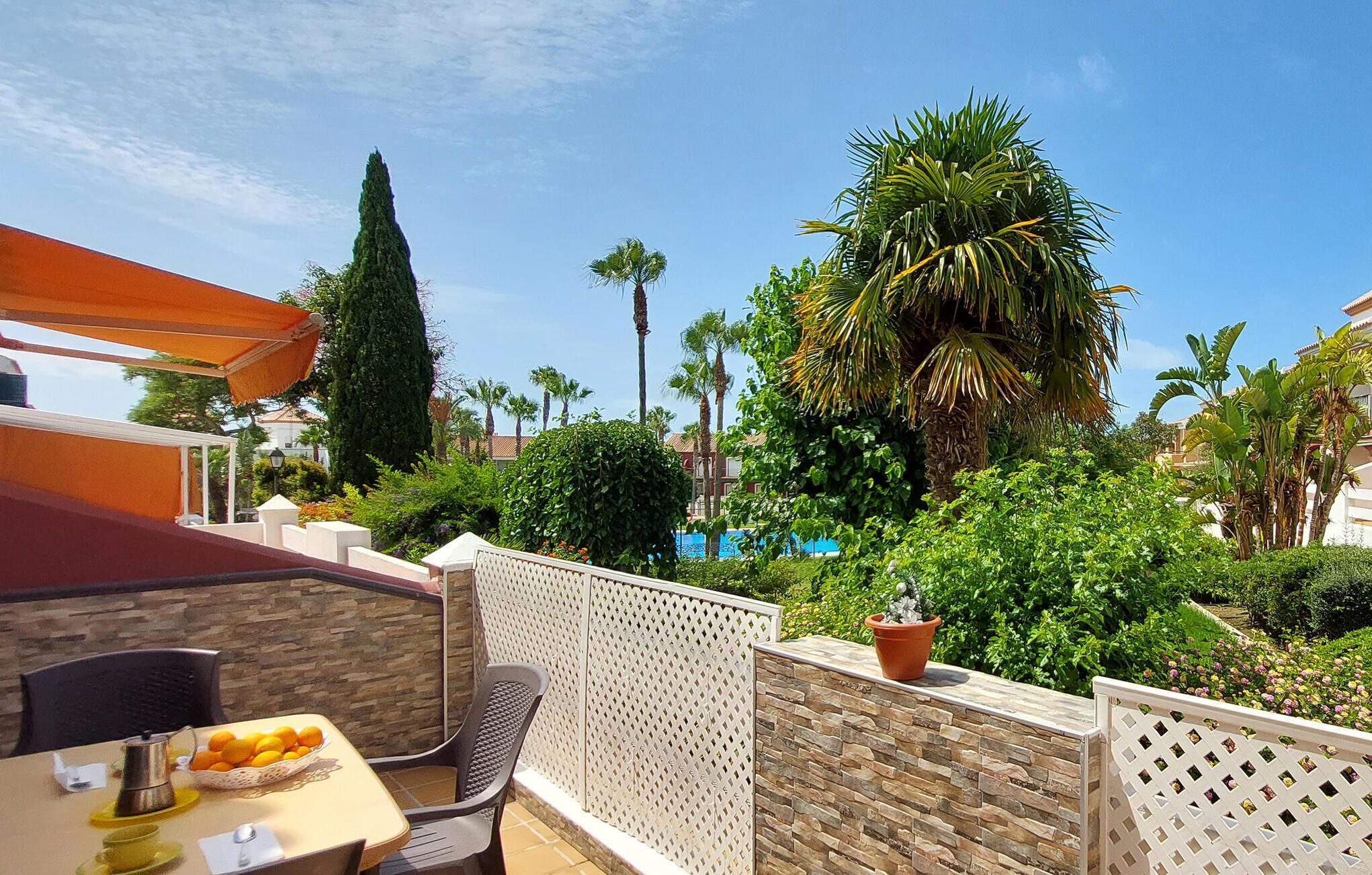 Eine Terrasse mit Esstisch, gedeckt für ein Frühstück, einer Steinmauer und Blick auf einen Pool und Palmen.