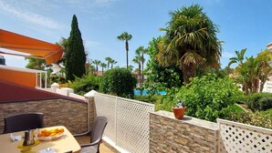 A patio area with a table set for breakfast, a stone wall, and a view of a pool and palm trees.