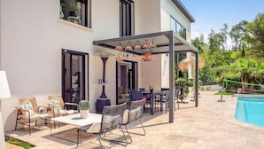Un patio exterior moderno con piscina, que cuenta con una pérgola, mobiliario para exteriores y una planta de cactus.