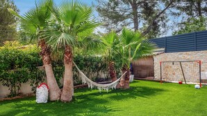 Un patio trasero bien cuidado con una hamaca, palmeras y una portería de fútbol.