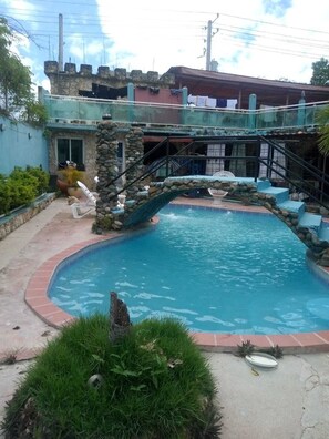 Una piscina con un puente de piedra, rodeada por un muro de piedra y vegetación.
