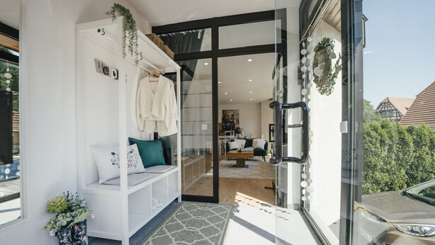 A modern entrance with a glass door, a white bench with cushions, and a decorative wreath. - APPARTIO - Modern country-style vacation apartment for 6 people (Ölbronn-Dürrn)