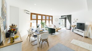 A modern living room with a dining area, a sofa, a TV, and a large window. - APPARTIO - Modern country-style vacation apartment for 6 people (Ölbronn-Dürrn)