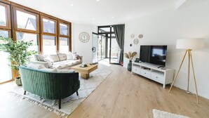 A modern living room with a sofa, coffee table, TV, and a large window. - APPARTIO - Modern country-style vacation apartment for 6 people (Ölbronn-Dürrn)
