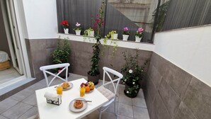 Un pequeño patio con una mesa blanca, dos sillas blancas y una variedad de macetas con plantas.