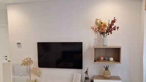 Una sala de estar moderna con un televisor de pantalla plana montado en la pared, un mueble blanco debajo y una pequeña estantería con adornos.