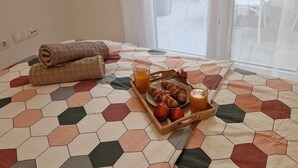 Una cama con una colcha de estampado hexagonal, una bandeja con croissants, manzanas y jugo de naranja, y toallas enrolladas sobre la cama.