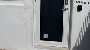 Una puerta blanca con un panel de vidrio, un letrero que dice 'NO ABRIR', una cámara de seguridad y una ventana con persianas.