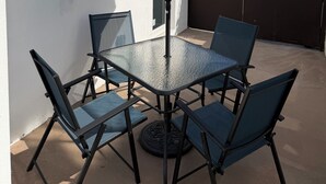 Un patio con una mesa y sillas, una sombrilla azul y una cerca marrón.