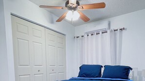 Un dormitorio con cama, armario blanco, ventilador de techo y cortinas blancas.