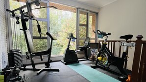 Une salle de sport à domicile équipée de matériel d’exercice, notamment un banc de musculation, un vélo d’appartement et un tapis de course.