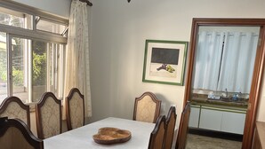 Une salle à manger avec une table dressée pour six personnes, des chaises en bois, un lustre, une fenêtre avec des rideaux et une œuvre d’art encadrée accrochée au mur.