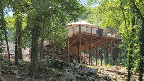 A rustic wooden structure with a roof, surrounded by trees and rocks.